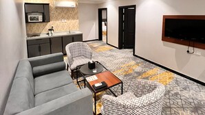 Een moderne woonkamer met een grijze bank, fauteuils met een patroon, een salontafel en een aan de muur bevestigde televisie.