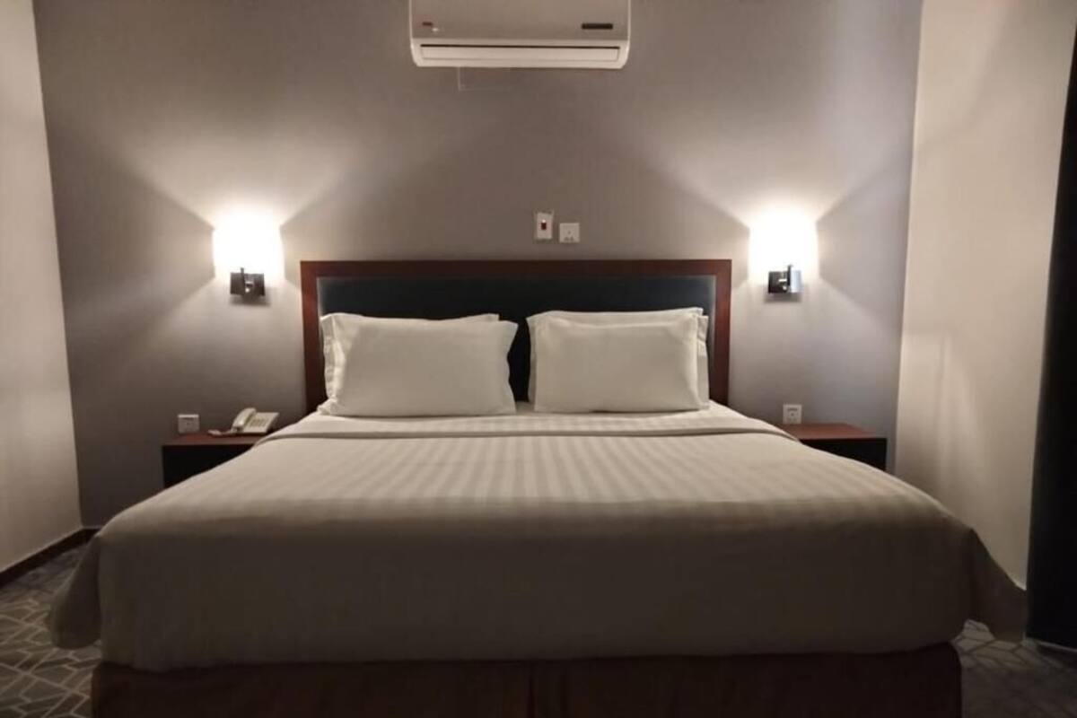 Een hotelkamer met een groot bed, twee nachtkastjes, een luchtverkoeler aan de muur en twee wandlampen.