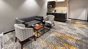 Een moderne zithoek met een bank, twee gestreept fauteuils, een salontafel en een keukenhoek met een magnetron.