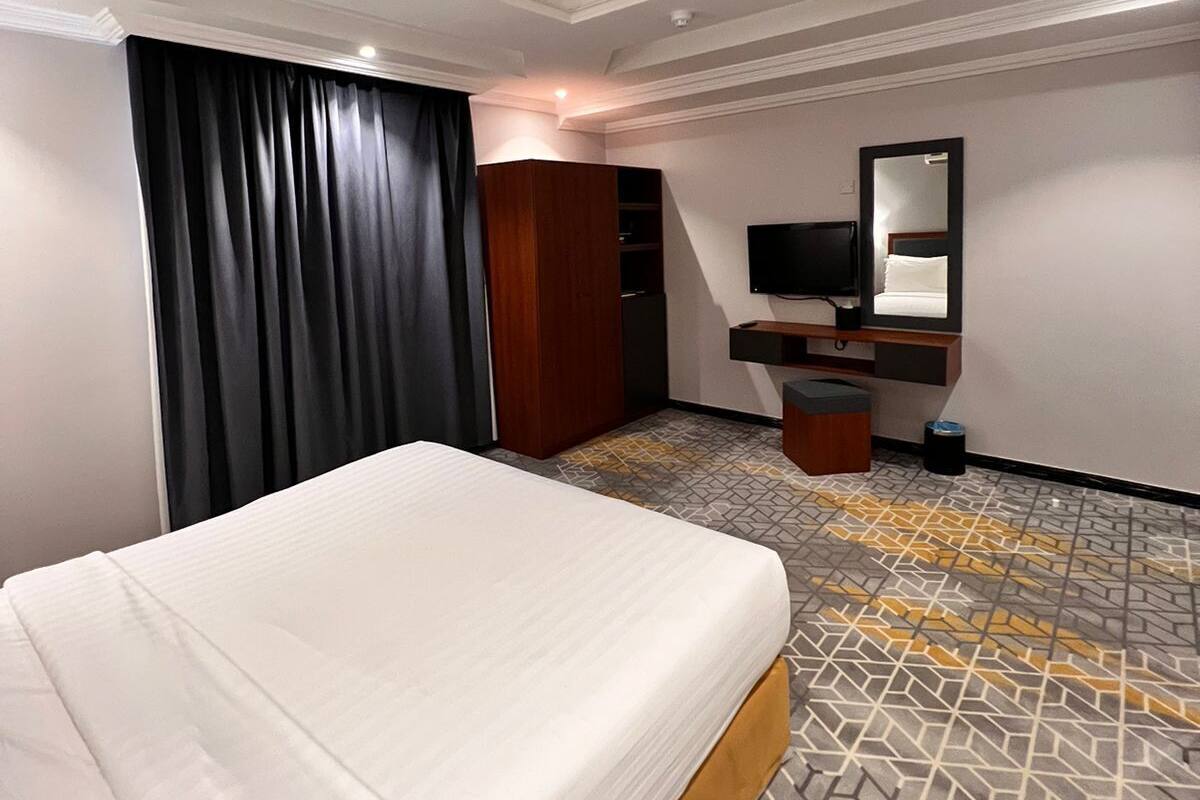 Hotellihuone, jossa on suuri sänky, vaatekaappi, peili, televisio ja kuviollinen matto.