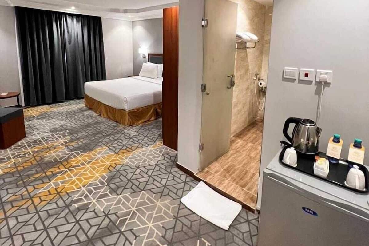Hotellihuone, jossa on sänky, pieni työpöytä, minibaari ja kylpyhuone, joka näkyy avoimesta ovesta.