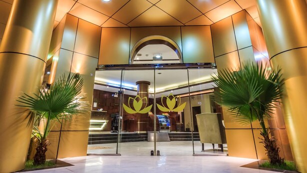 Una entrada de hotel moderna con puerta de cristal, pilares grandes y una palmera al frente.