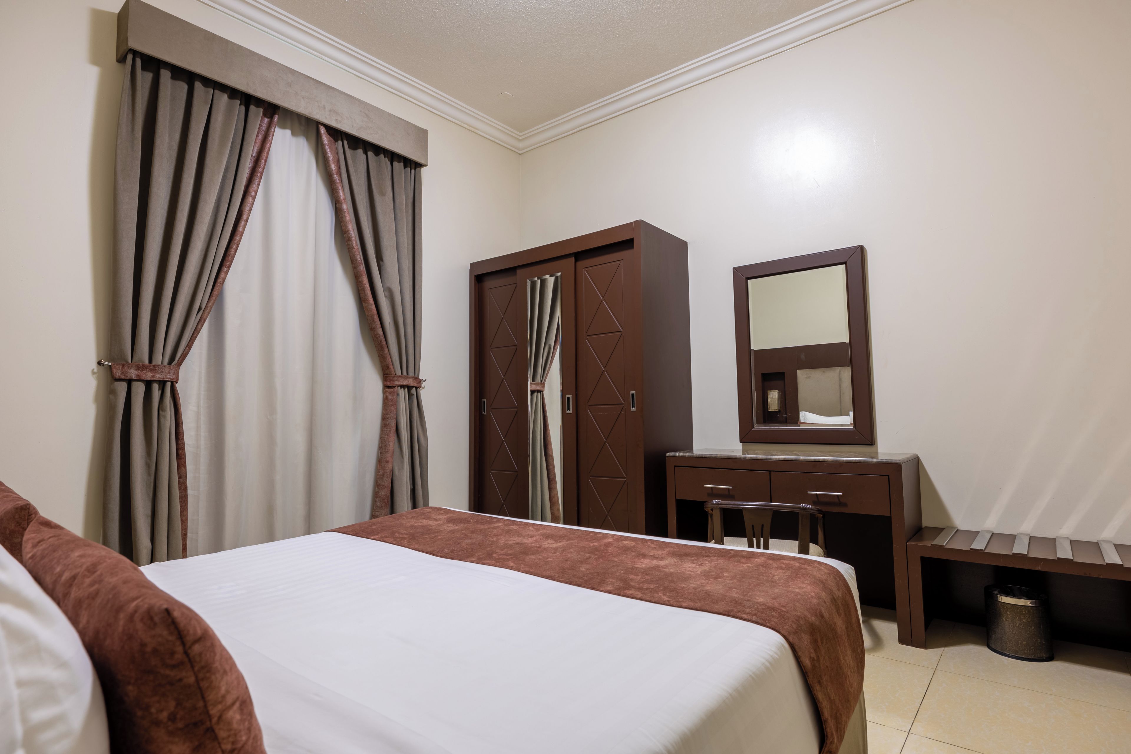 A hotel room with a bed, a wardrobe, a mirror, and a bench.