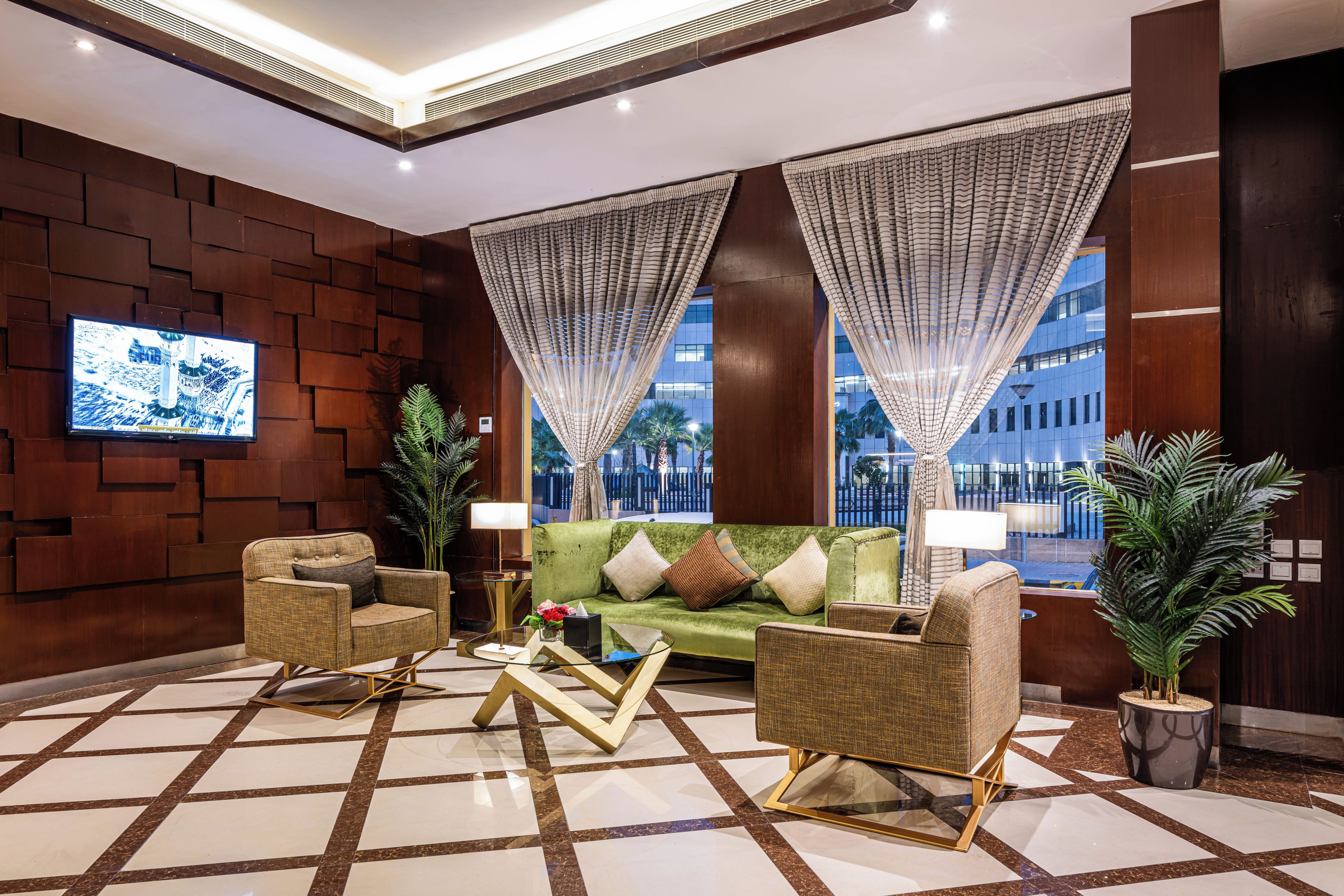 A lobby with a green sofa, two armchairs, a coffee table, and a TV on the wall.