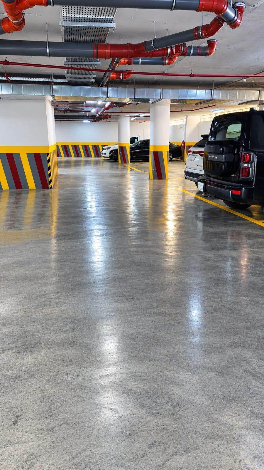 A parking garage with concrete floors, yellow and red striped columns, and red and gray pipes on the ceiling.