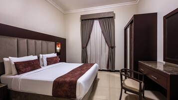 A hotel room with a large bed, a desk, a chair, a wardrobe, and a window with curtains.