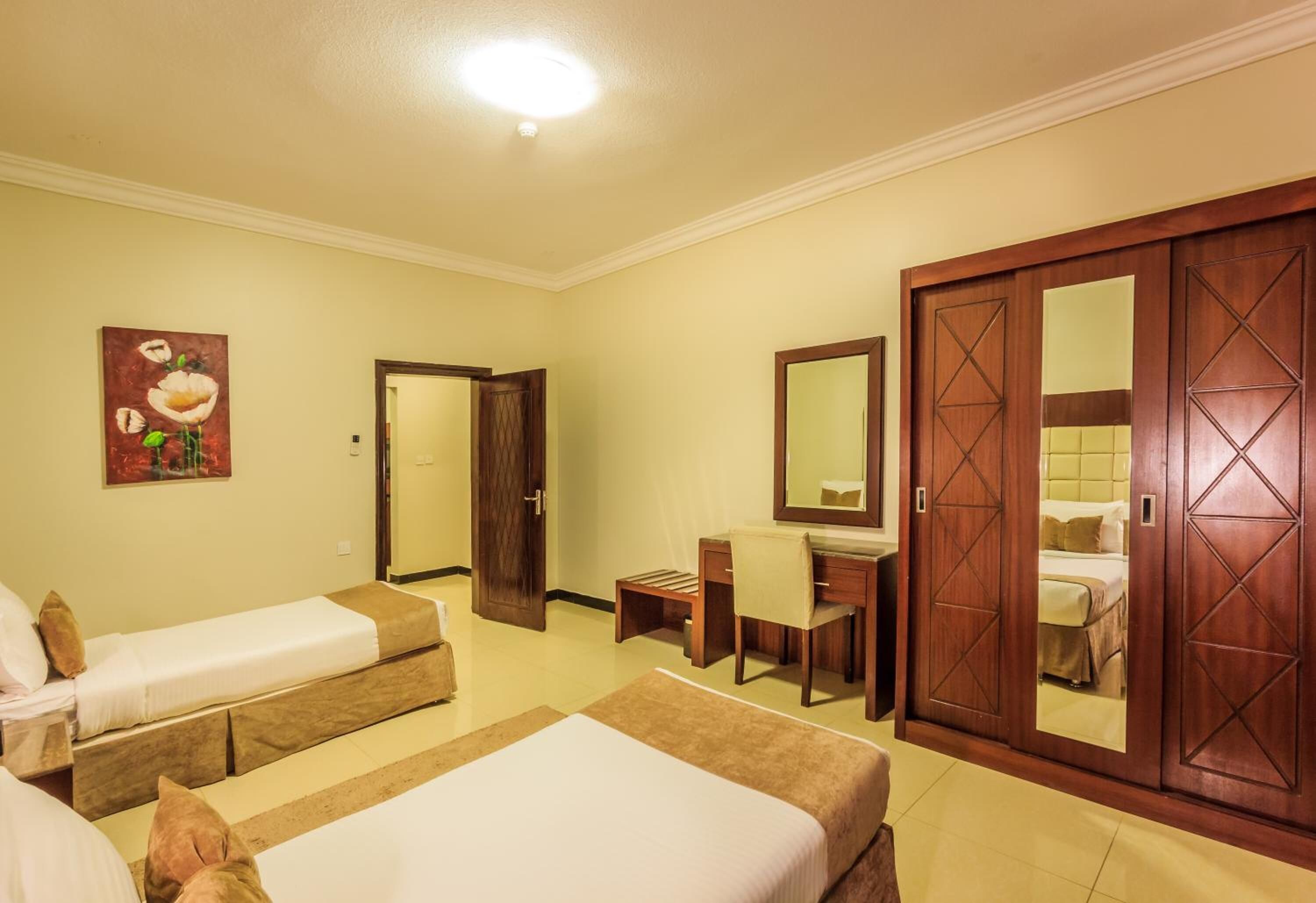 A hotel room with two single beds, a desk with a chair, a large mirror, and a wardrobe.