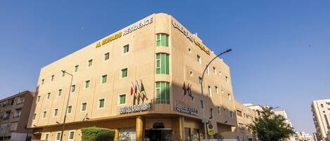 A multi-story hotel with a prominent sign reading 'Al Muhajid Residence' and 'Serviced Apartments'.