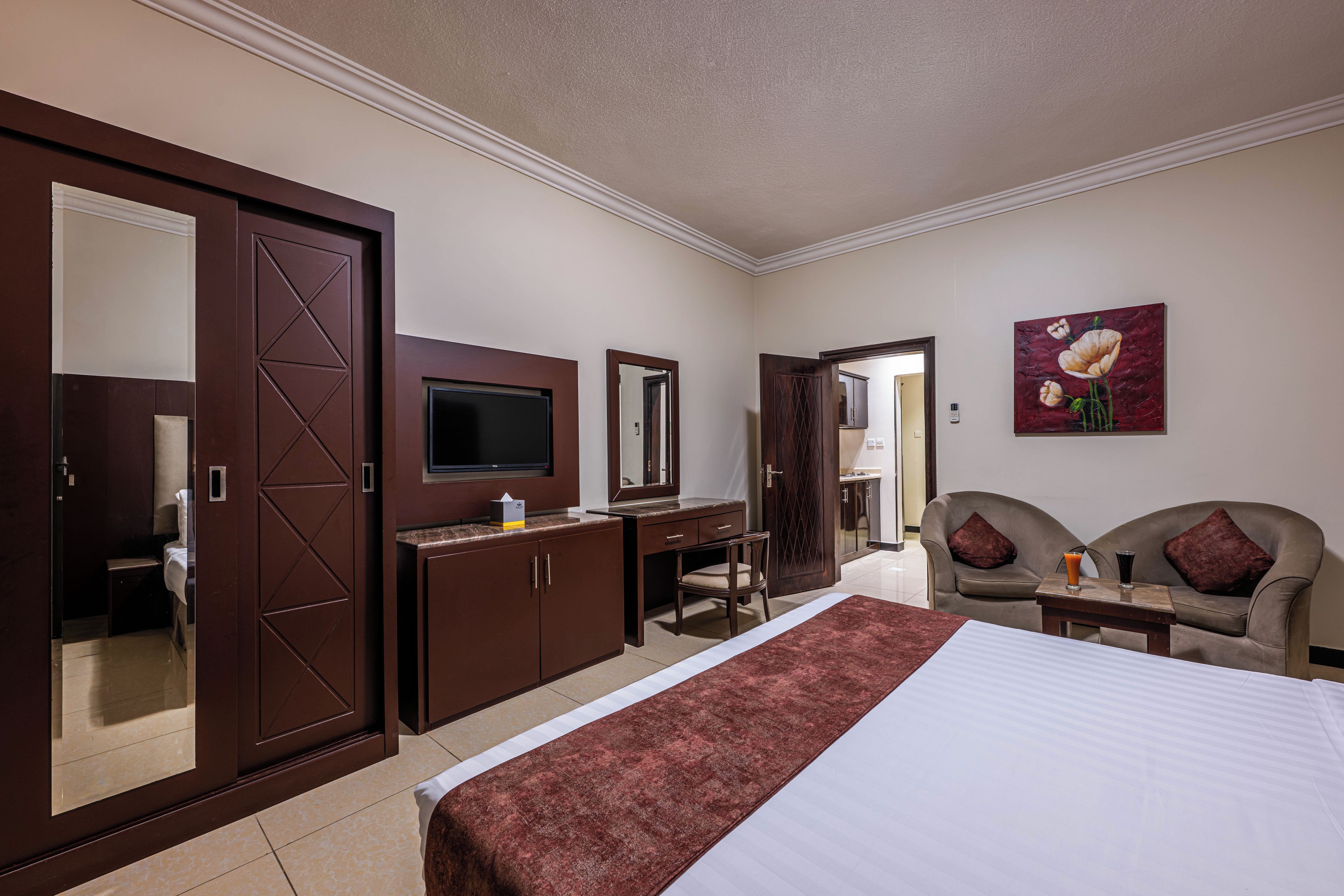 Una habitación de hotel con cama, escritorio, televisor, armario y una zona de estar con dos sillas.