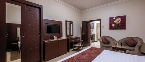 Una habitación de hotel con cama, escritorio, televisor, armario y una zona de estar con dos sillas.