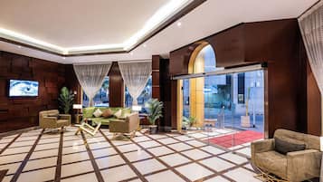 A hotel lobby with a checkered floor, seating area, television, and a glass entrance.