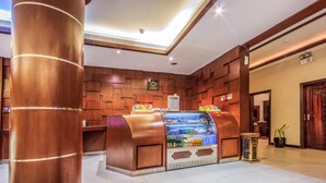 Un vestíbulo de hotel con una estación de bebidas de autoservicio, paneles de madera y una mesa de recepción.