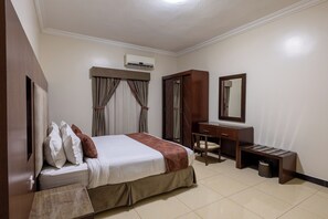 Quarto de hotel com cama, escrivaninha, cadeira, guarda-roupa e ar condicionado.