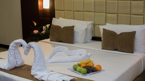 Habitación de hotel con dos camas, cada una con sábanas blancas y almohadillas marrones. Hay una bandeja de frutas sobre la cama en primer plano.