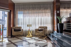Eine Hotelhalle mit zwei Sesseln, einem Glastisch, einer Zimmerpflanze und einer Rezeption.