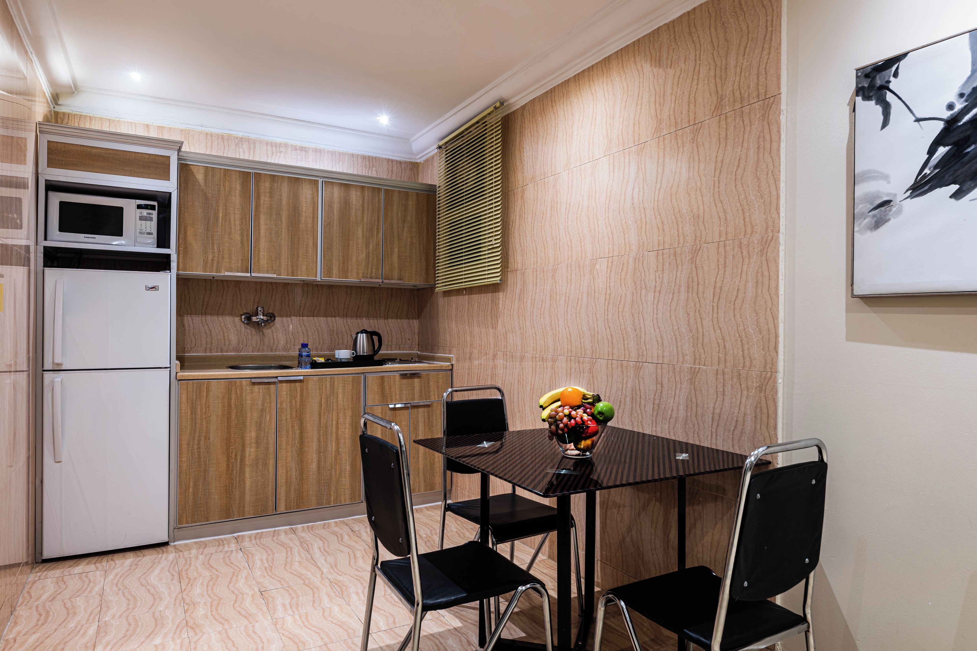 A compact kitchen with a microwave, refrigerator, and a sink. There's a dining table with chairs and a fruit bowl on it.