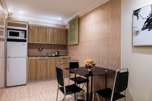 A compact kitchen with a microwave, refrigerator, and a sink. There's a dining table with chairs and a fruit bowl on it.