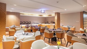 A modern hotel dining area with round tables and orange chairs, a central bar, and wooden paneling on the walls. - Al Muhaidb Residence Al ASKARY - Economic (Riyadh)