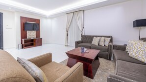A modern living room with a flat-screen TV, a wooden entertainment unit, and two sofas with patterned cushions. - Al Muhaidb Residence Al ASKARY - Economic (Riyadh)