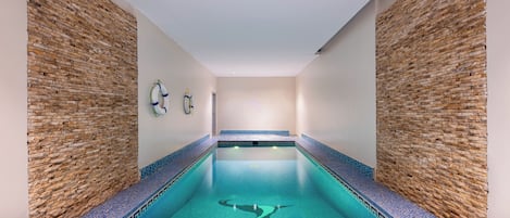 A swimming pool with mosaic tile edges, surrounded by stone walls, and equipped with a lifebuoy and a paddle on the wall.