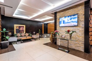 A modern lobby with a seating area, a television mounted on a stone wall, and a staircase leading to an upper level.
