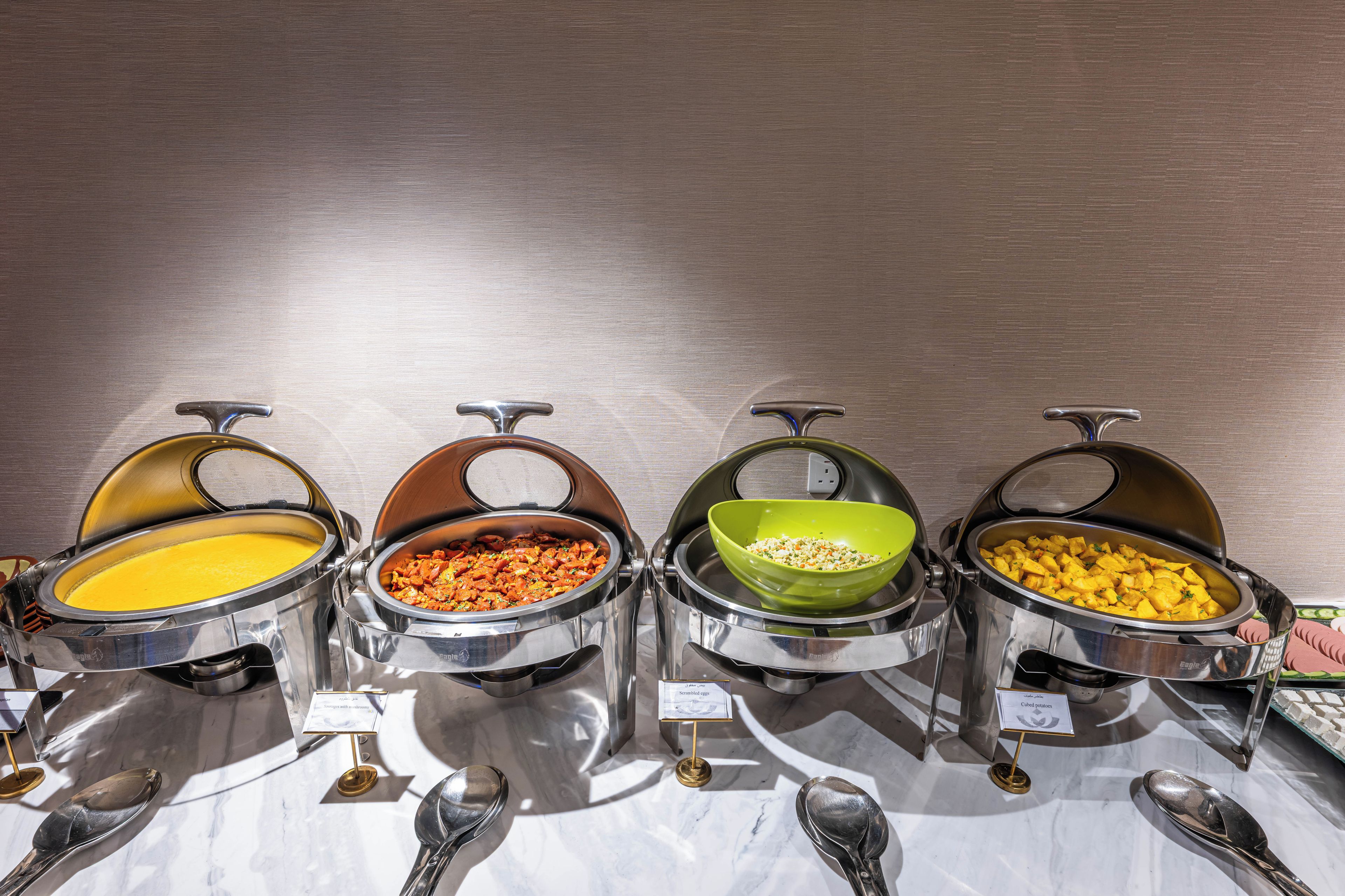 A buffet with four different food options, each in a separate bowl with a label.