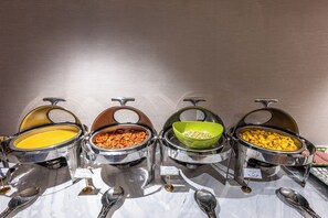 Ein Buffet mit vier verschiedenen Speisen, jede in einer separaten Schale mit Beschriftung.