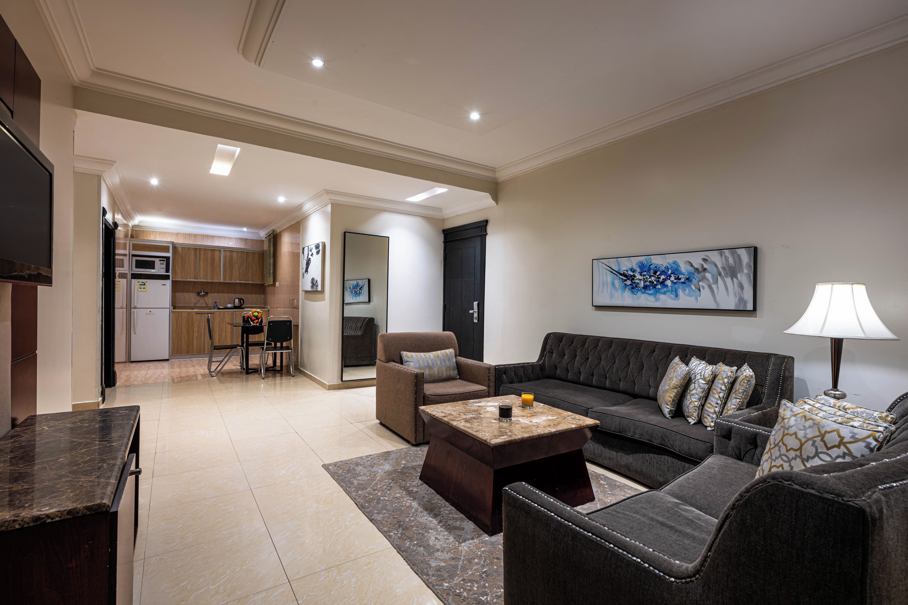 A modern living room with a sofa, armchairs, a coffee table, and a dining area with a kitchen in the background.