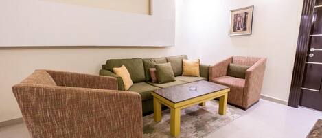 Una sala de estar con un sofá, dos sillones, una mesita de centro y un cuadro enmarcado en la pared.