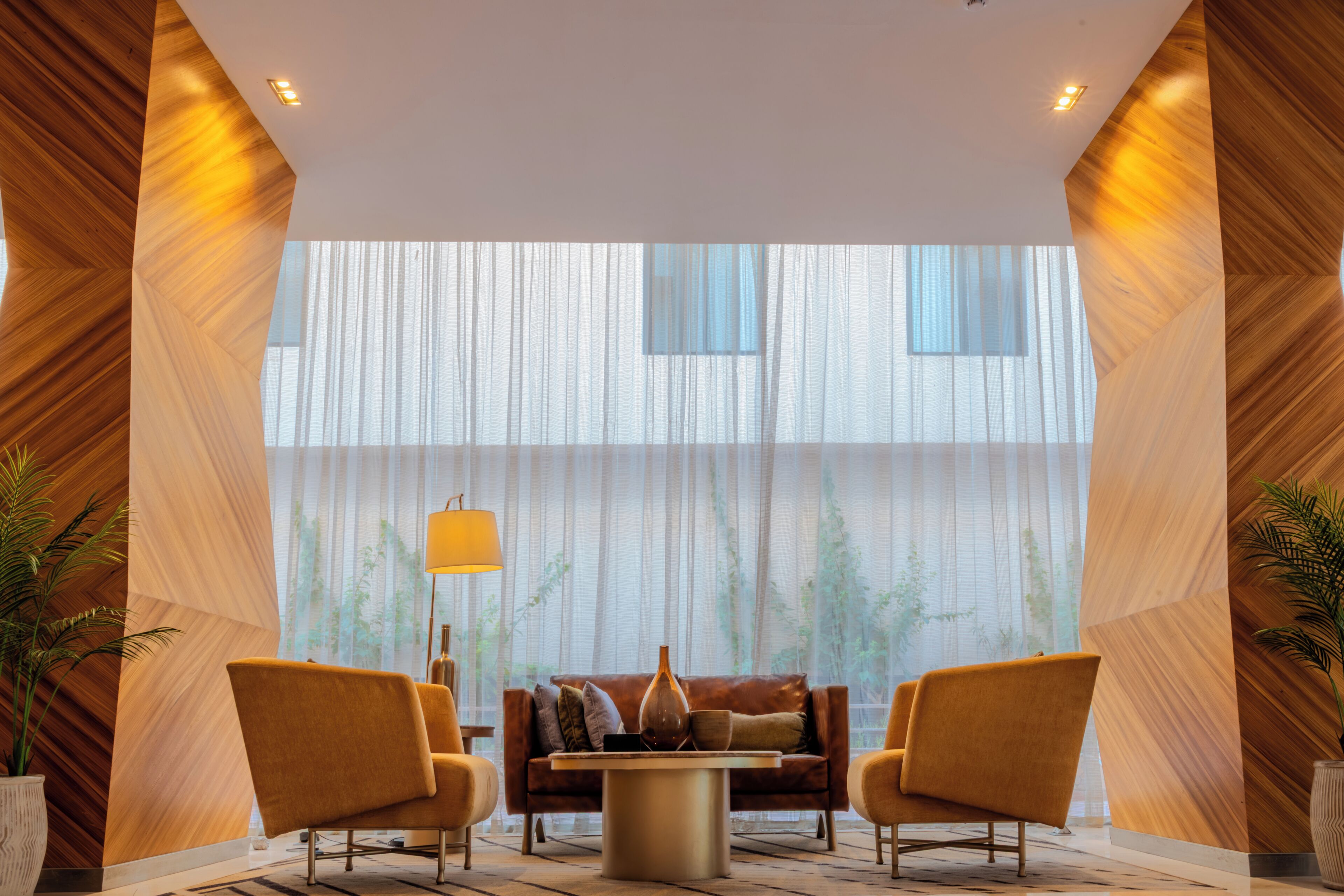 A modern lobby with a sofa, two armchairs, a coffee table, and a large window with vertical blinds.
