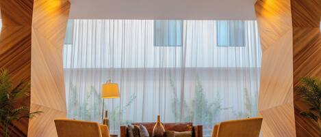 A modern lobby with a sofa, two armchairs, a coffee table, and a large window with vertical blinds.