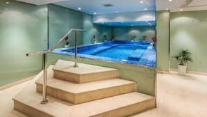 Una piscina interna moderna con pareti di vetro trasparente, una scala in metallo che conduce alla piscina e piante in vaso intorno all'area.