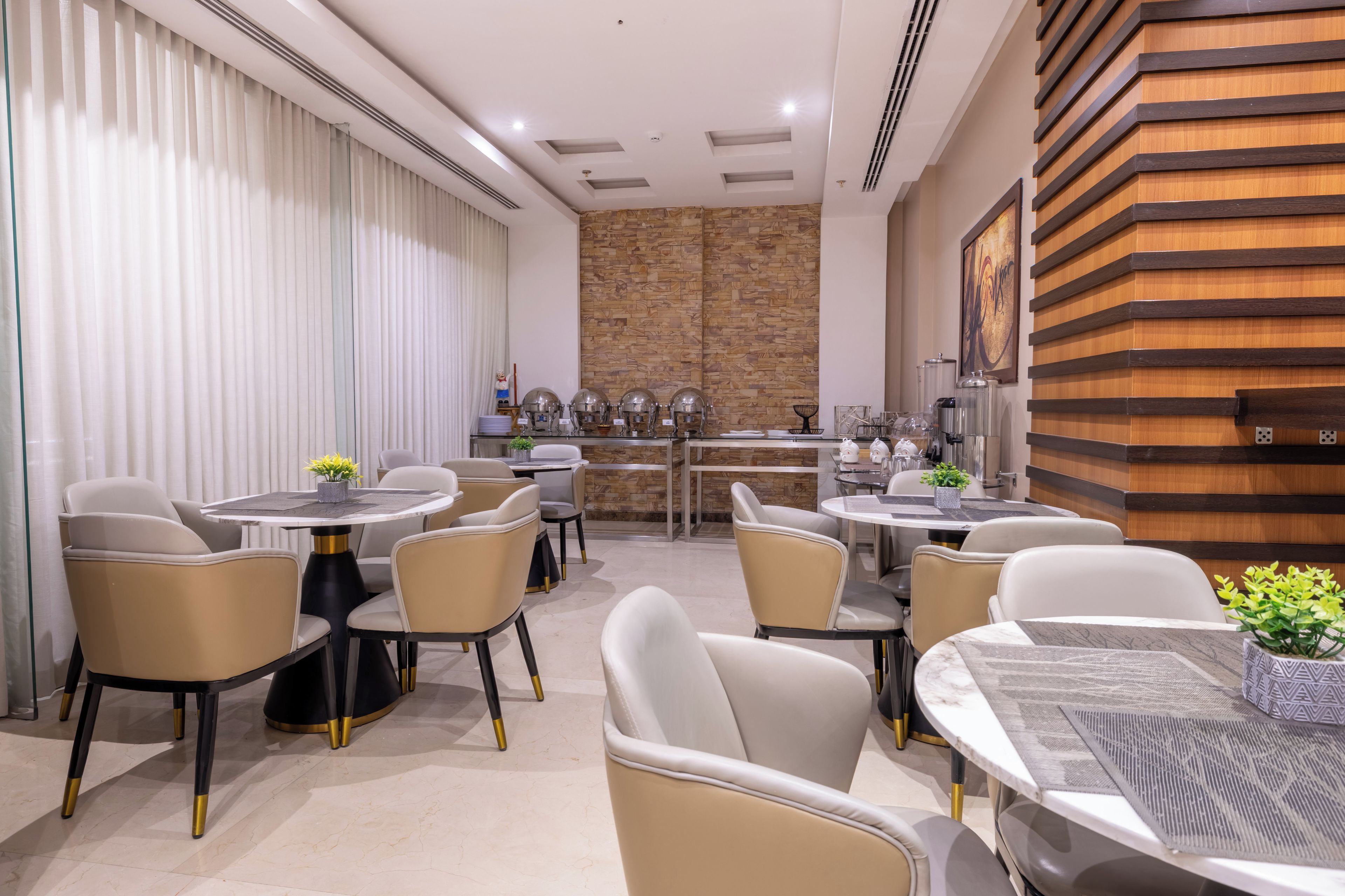 A modern dining area with round tables and chairs, a kitchen in the background, and a wooden accent wall.