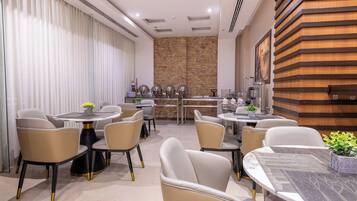 A modern dining area with round tables and chairs, a kitchen in the background, and a wooden accent wall.