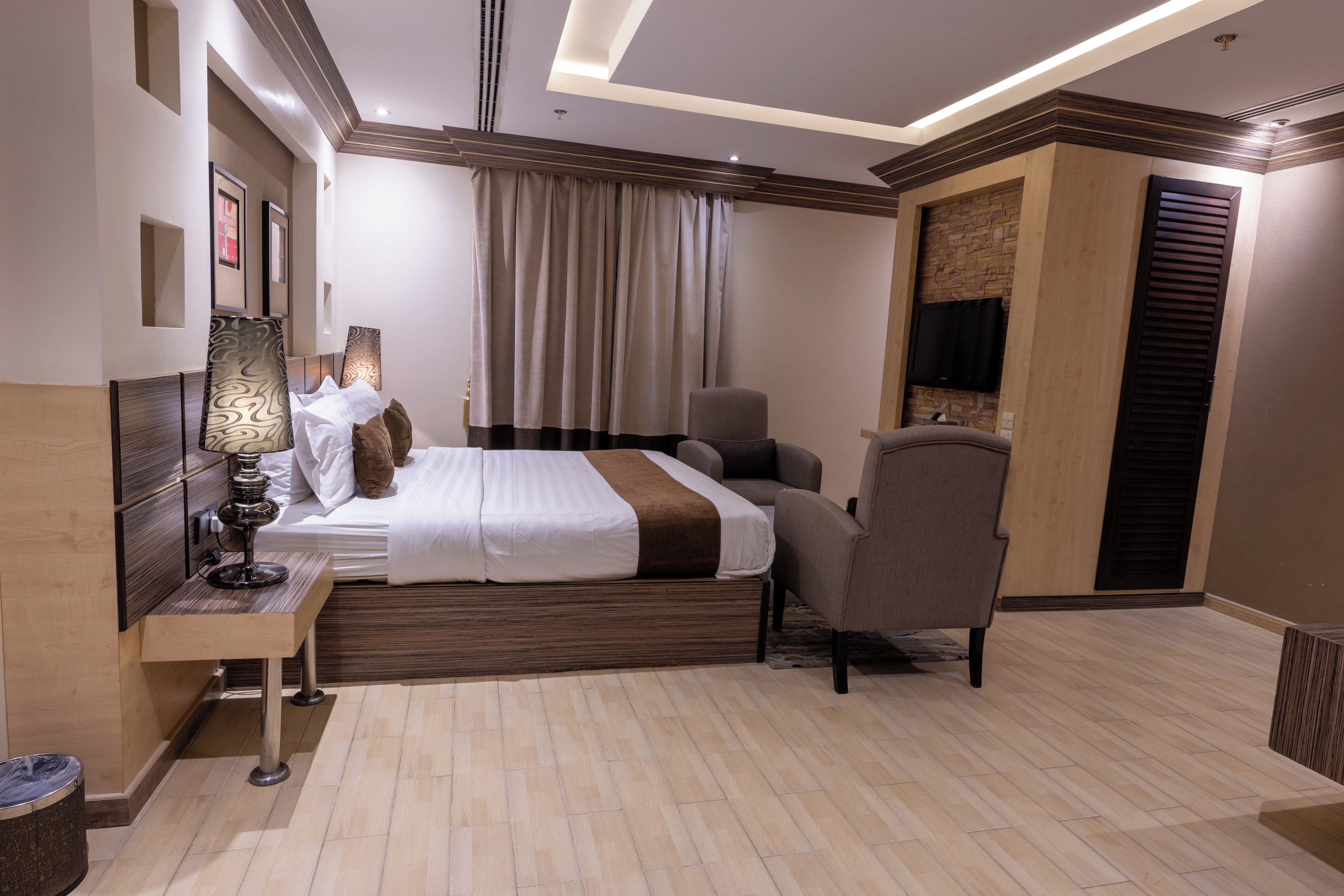 Una habitación de hotel moderna con una cama bien hecha, un escritorio con lámpara, una silla y un televisor montado en la pared.
