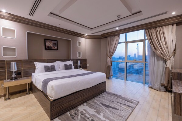 A modern bedroom with a large bed, a city view, and a wooden headboard. - Al Muhaidb Residence Al Malaz 5 - Economic (Riyadh)