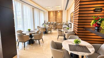 A hotel dining area with round tables and chairs, a stone accent wall, and a wooden panel wall.