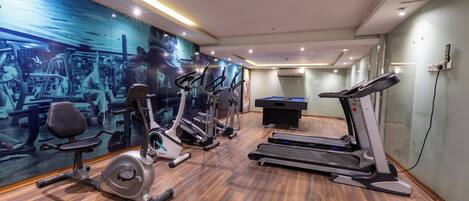 Un gimnasio con equipo de ejercicio, una mesa de billar y un amplio mural motivacional.