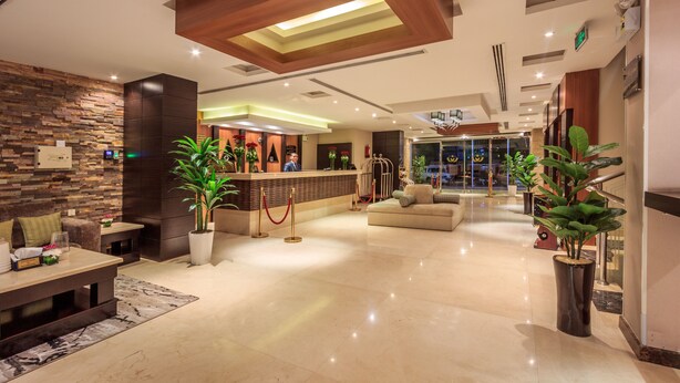 Una moderna hall d'albergo con reception, area salotto e una scala che conduce a un piano superiore.