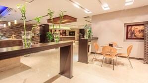 Una hall d'albergo moderna con reception, area salotto e piante ornamentali.