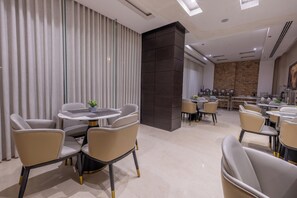 A modern dining area with round tables and chairs, a large window with curtains, and a stone wall in the background. - Al Muhaidb Residence Al Malaz 5 - Economic (Riyadh)