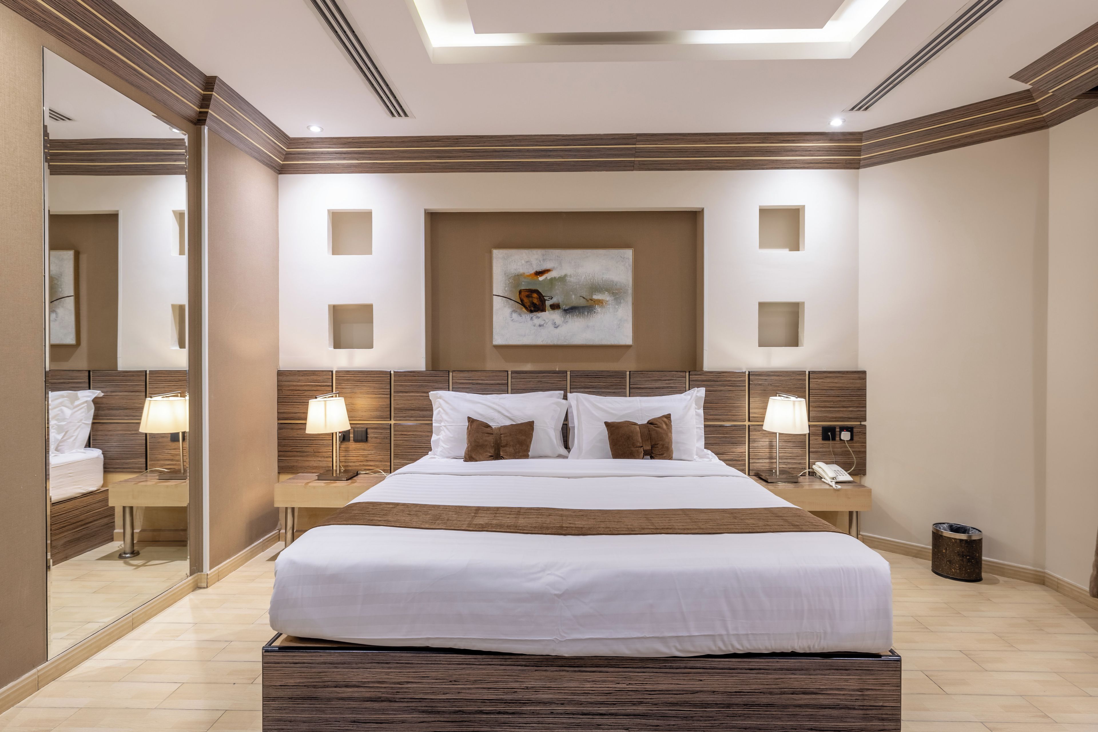 A hotel room with a large bed, two bedside tables with lamps, a wall-mounted painting, and a mirror.