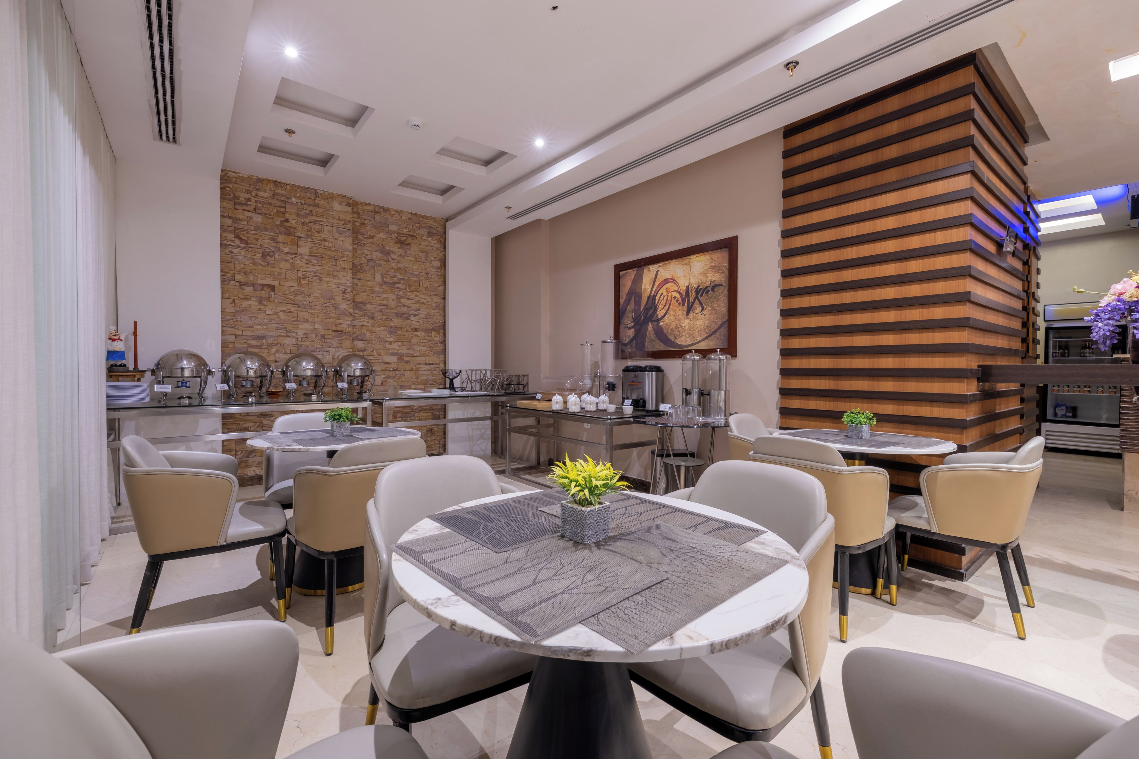 A modern dining area with round tables, cushioned chairs, and a kitchen in the background.
