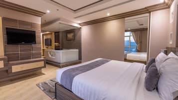 A modern bedroom with a large bed, a flat-screen TV, a vanity with a mirror, and a view of the city through a window.