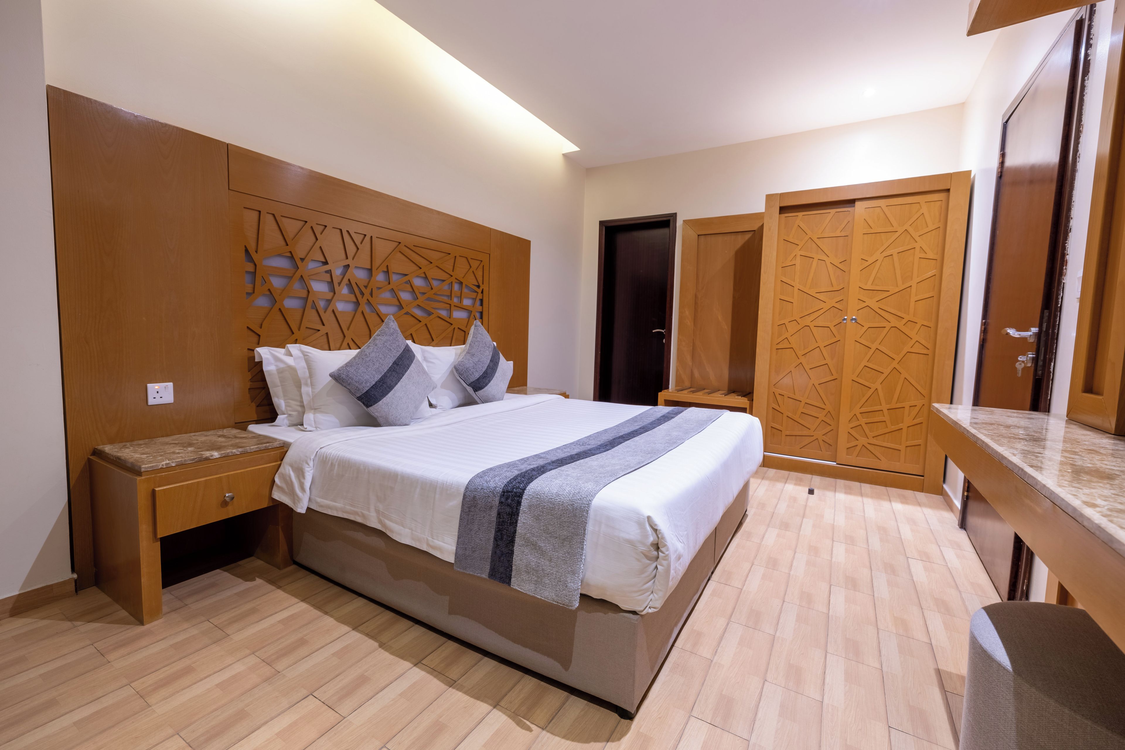 Une chambre d’hôtel avec un grand lit, une tête de lit en bois, une table de chevet, un bureau et une armoire.