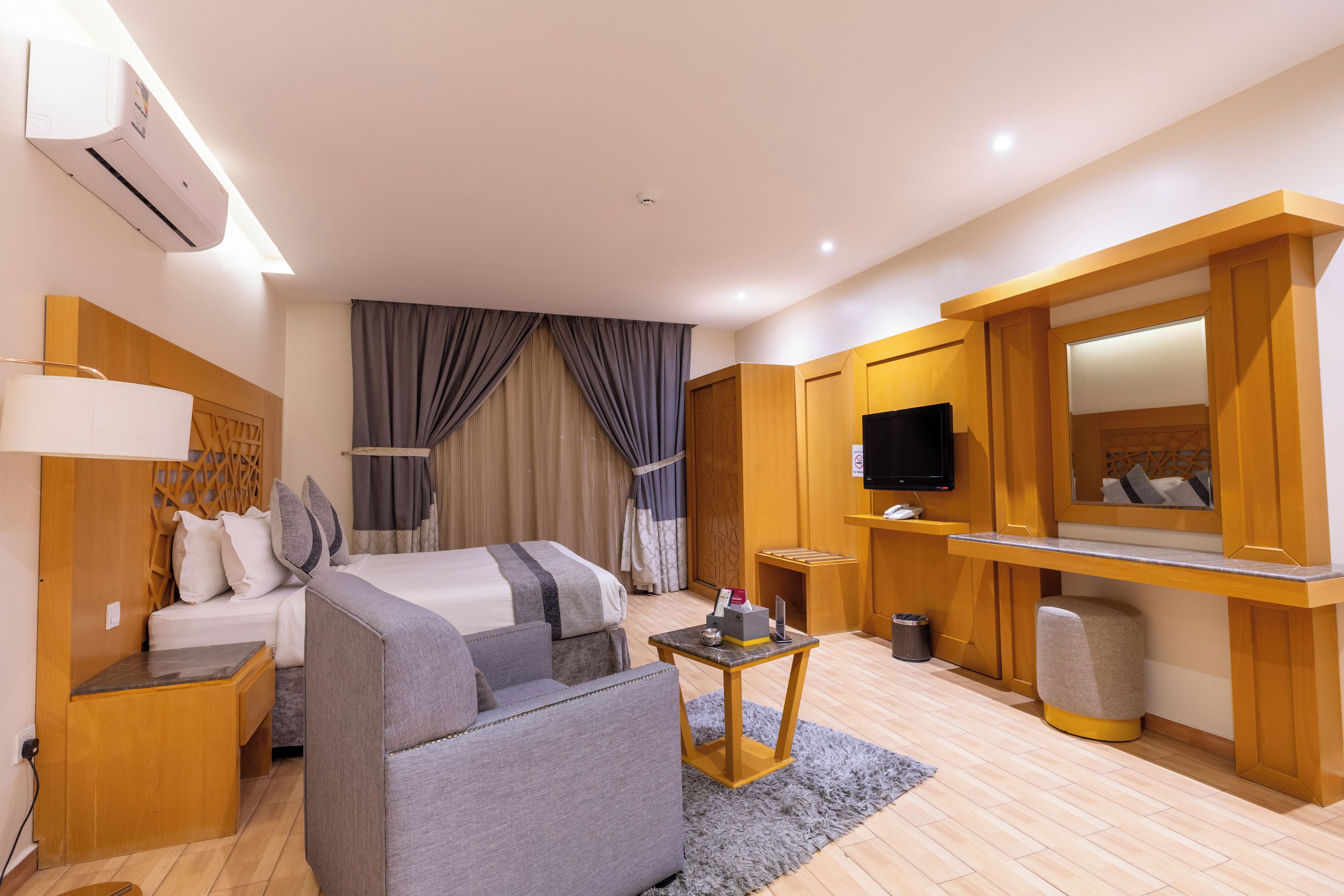 Una habitación de hotel con cama, sofá, televisor, una mesita y un espejo.