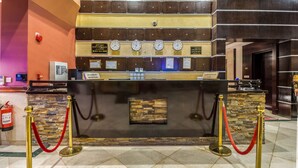 A hotel reception area with a stone wall, a reception desk, and multiple clocks.