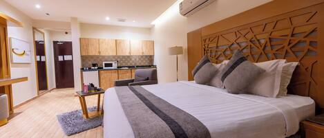 Una habitación de hotel con una cama grande, un escritorio, una kitchenette y un baño.