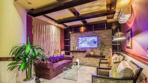A modern lobby with a leather sofa, a glass coffee table, a potted plant, a fire extinguisher, and a mounted television.