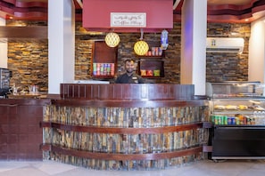 A coffee shop counter with a stone mosaic backsplash, a sign above indicating it's a coffee shop, and a variety of snacks and drinks on display. - Al Muhaidb Residence Al Malaz 4 - Economic (Riyadh)